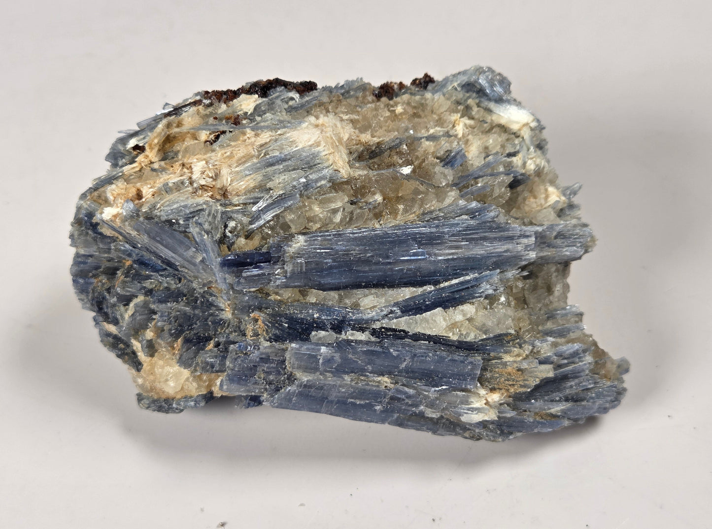 A natural mineral specimen showing blue-gray tabular crystals with a beige and white matrix, photographed on a neutral light gray background.