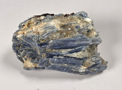 A natural mineral specimen showing blue-gray tabular crystals with a beige and white matrix, photographed on a neutral light gray background.