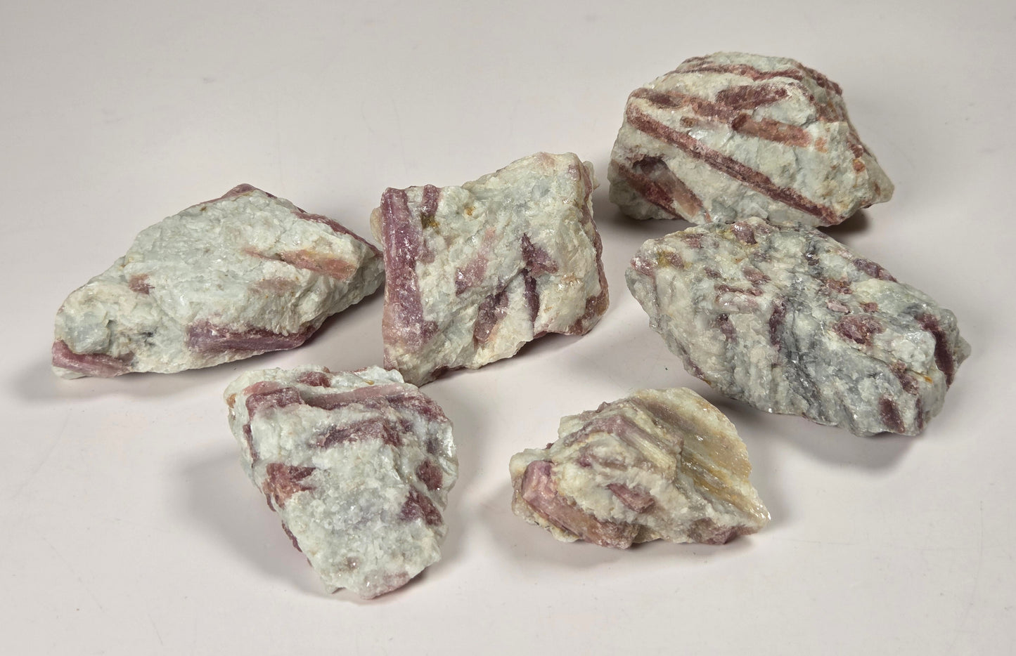 Six rough mineral or stone pieces with a pale grayish-white surface and reddish-brown veining, arranged on a plain light background.