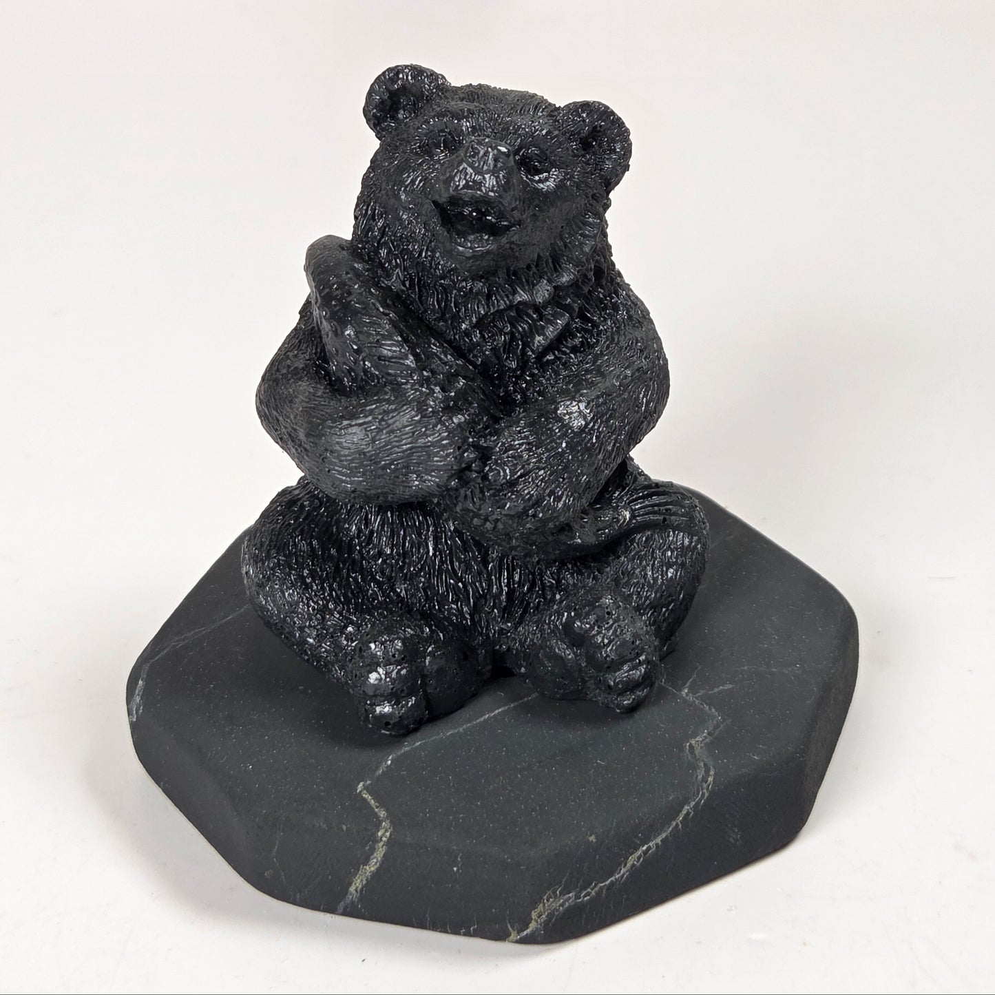 A small black bear figurine sitting on a dark gray stone base, photographed against a plain light background.