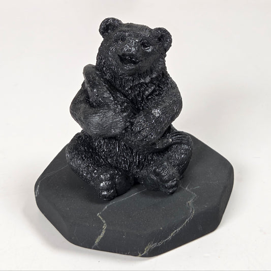 A small black bear figurine sitting on a dark gray stone base, photographed against a plain light background.