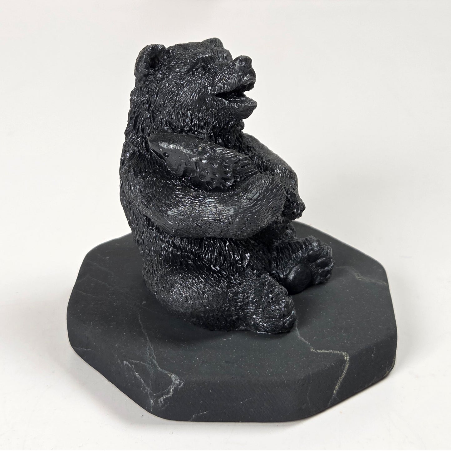 A small black bear figurine sitting upright on a dark gray stone base, photographed against a plain light background.