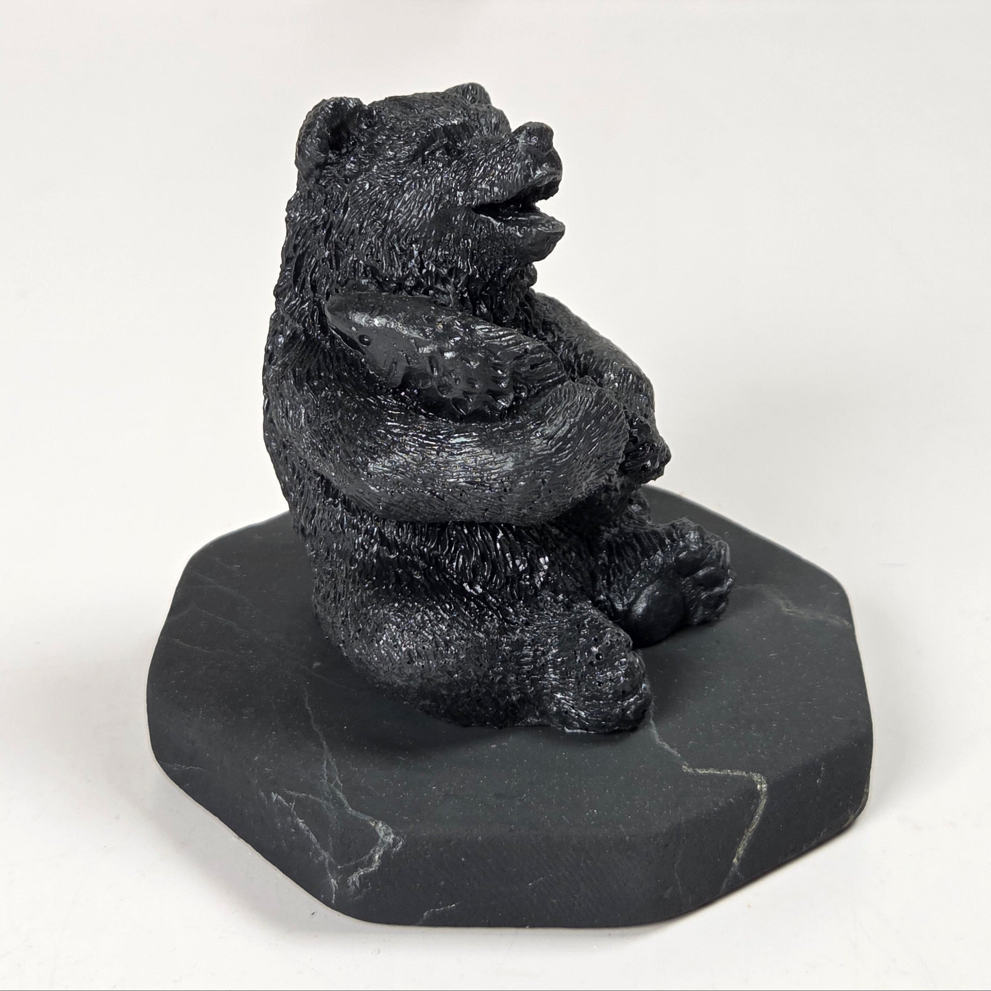 A small black bear figurine sitting upright on a dark gray stone base, photographed against a plain light background.