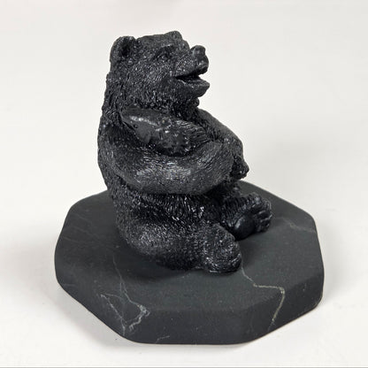 A small black bear figurine sitting upright on a dark gray stone base, photographed against a plain light background.