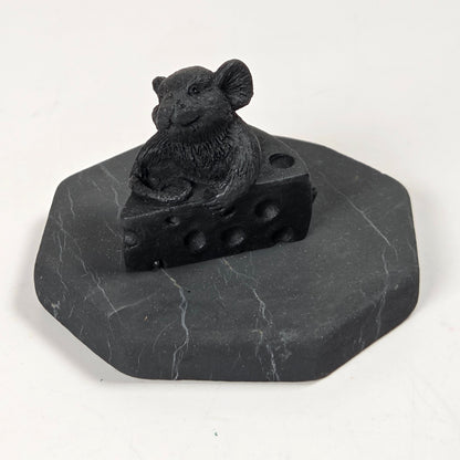 A black mouse figurine sitting on a wedge of cheese, mounted on an octagonal dark gray stone base, photographed against a plain white background.