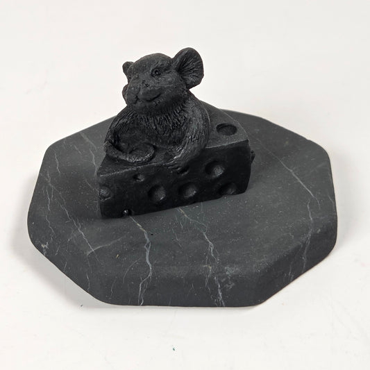 A black mouse figurine sitting on a wedge of cheese, mounted on an octagonal dark gray stone base, photographed against a plain white background.