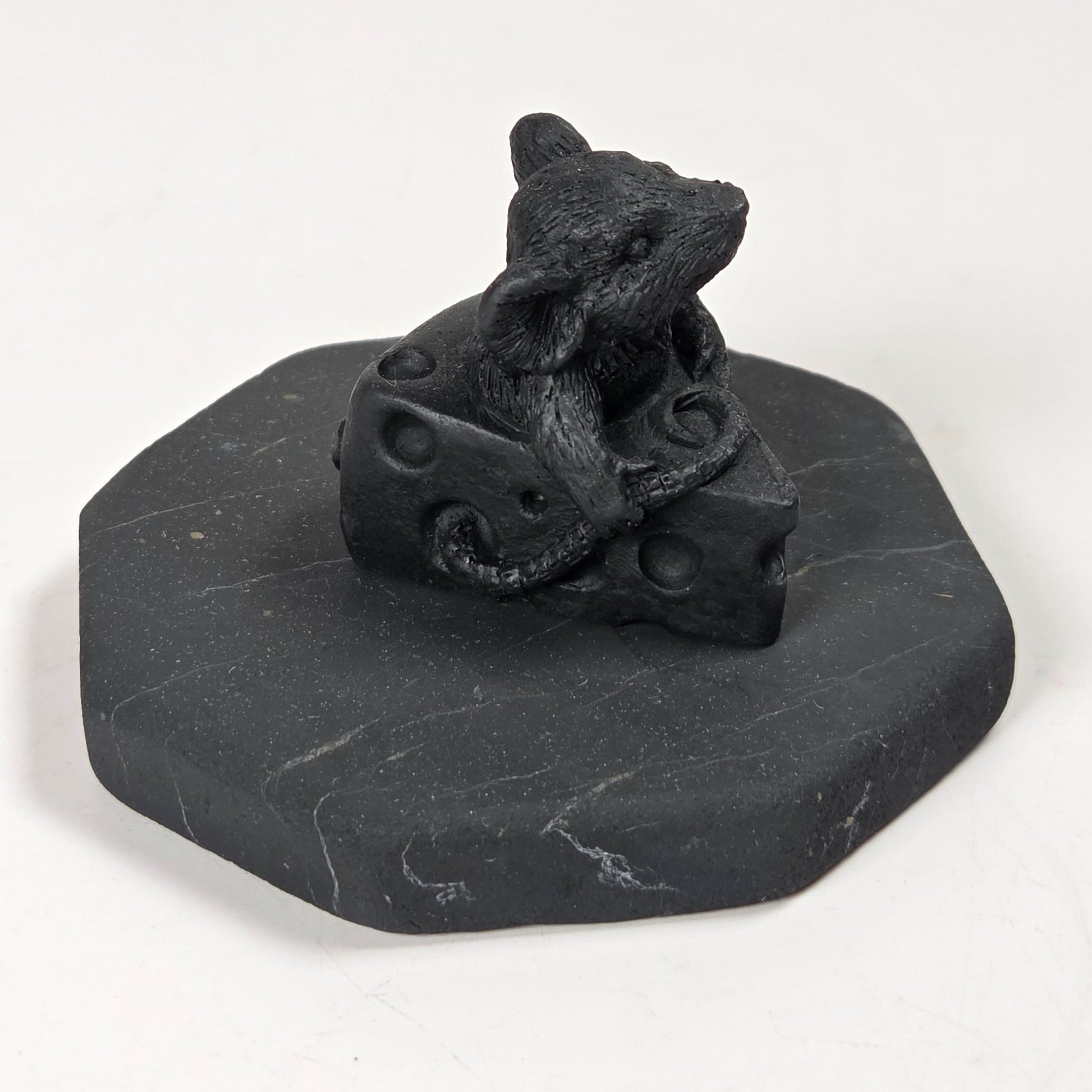 A small black figurine of a mouse sitting on a block of cheese, mounted on a dark gray octagonal base, photographed on a plain white background.