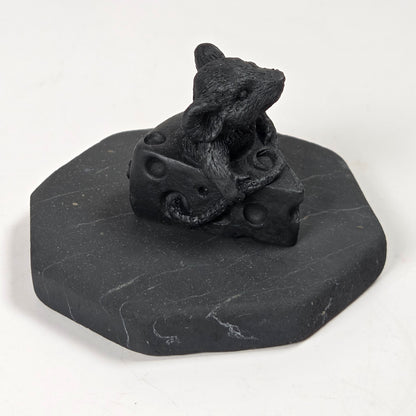 A small black figurine of a mouse sitting on a block of cheese, mounted on a dark gray octagonal base, photographed on a plain white background.