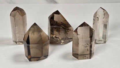 Five smoky quartz crystal points of varying heights arranged on a white surface with a light gray marble-patterned background.