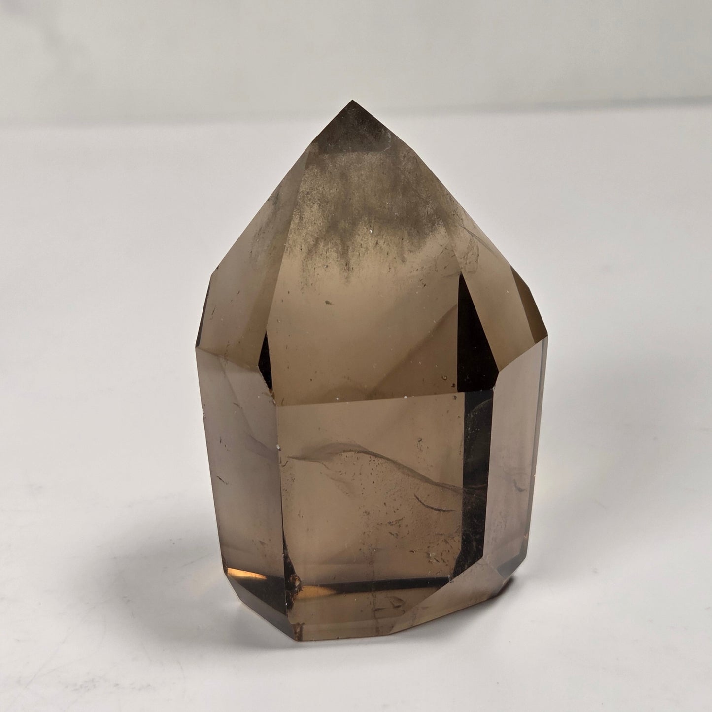 A faceted smoky quartz crystal point, showing natural internal inclusions and a translucent brown-gray color, photographed on a light gray surface.