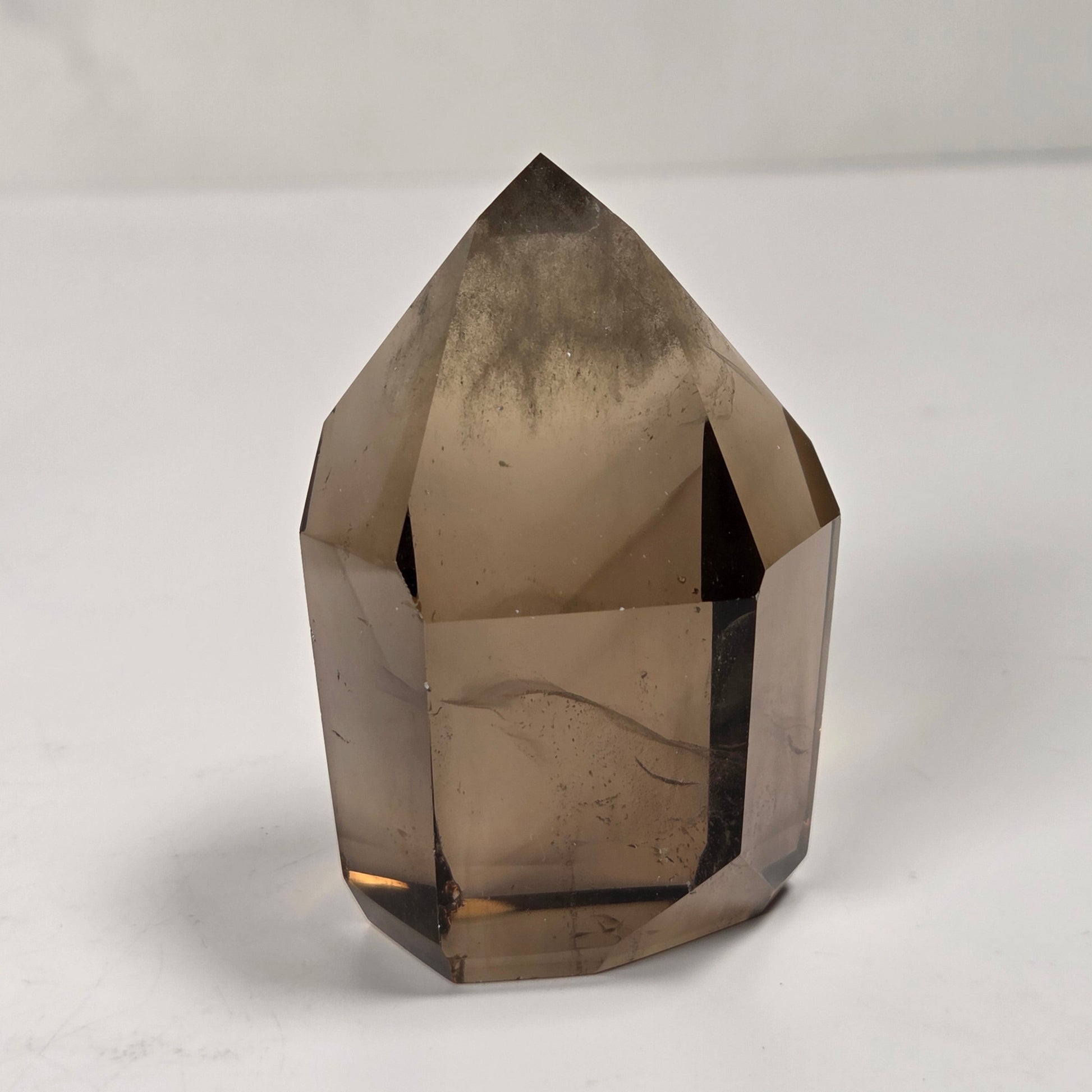 A faceted smoky quartz crystal point, showing natural internal inclusions and a translucent brown-gray color, photographed on a light gray surface.
