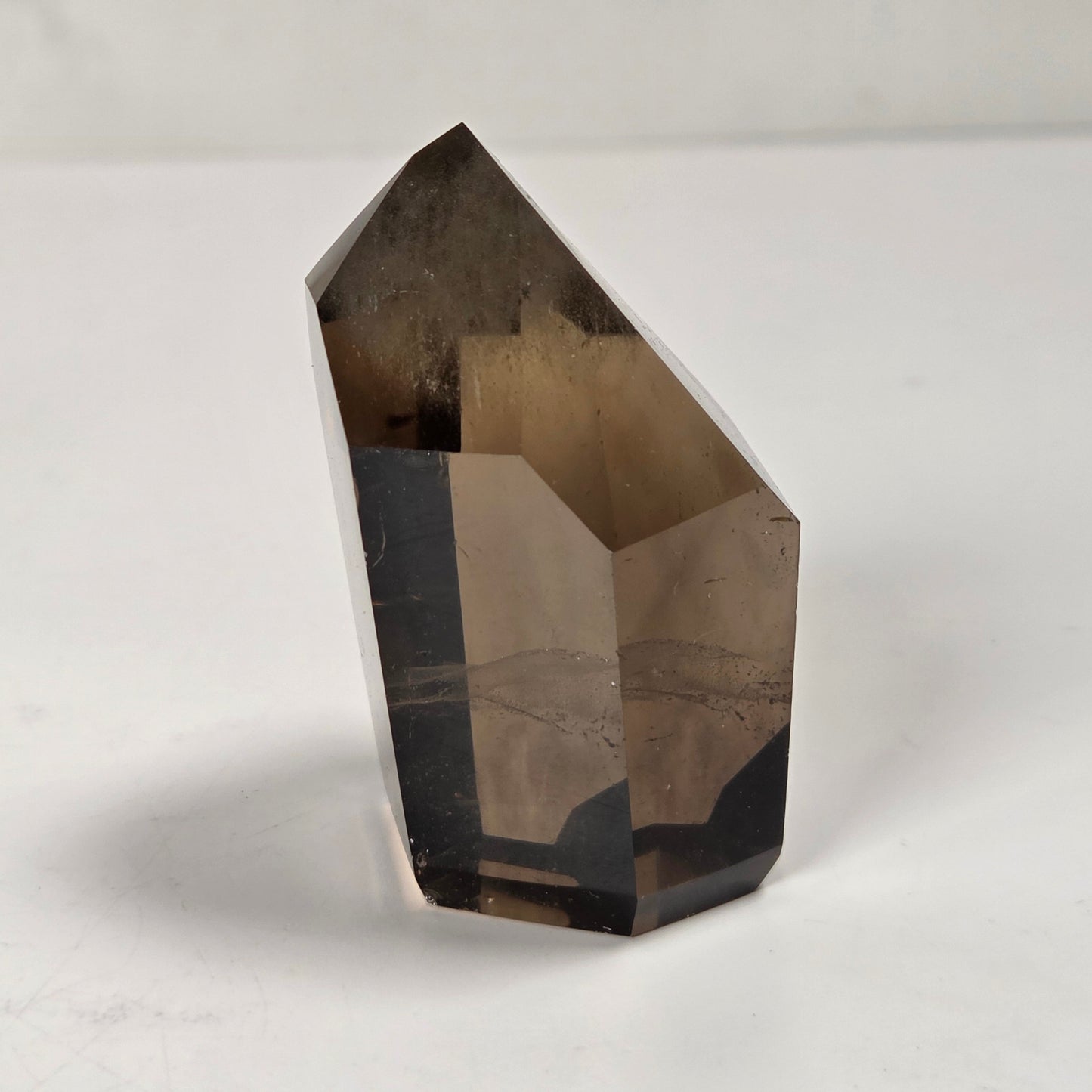 A natural smoky quartz crystal point with a hexagonal shape, standing upright on a light gray surface with a soft shadow.