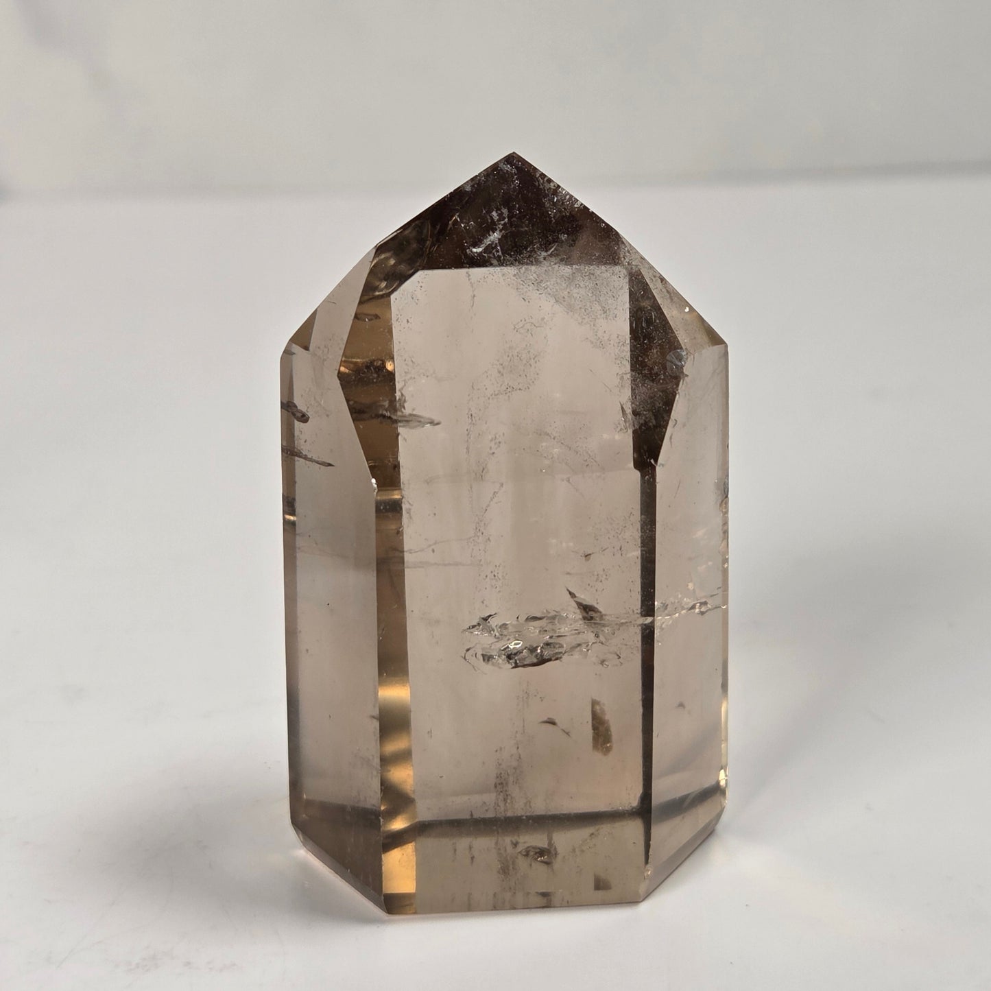 A natural smoky quartz crystal point with a pointed top, standing upright on a light gray surface.