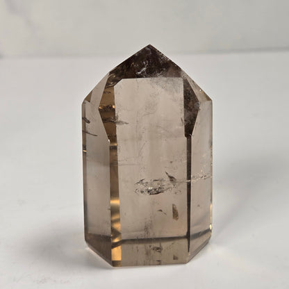A natural smoky quartz crystal point with a pointed top, standing upright on a light gray surface.