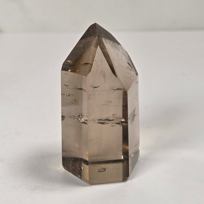 A natural smoky quartz crystal point with a faceted geometric structure, standing upright on a light gray surface.