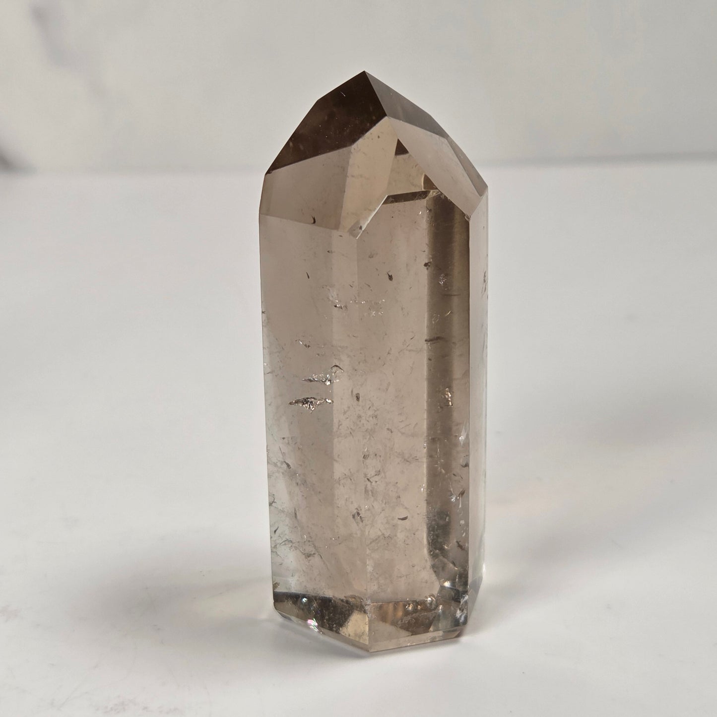 A natural smoky quartz point crystal standing upright on a light gray surface against a white marble background.