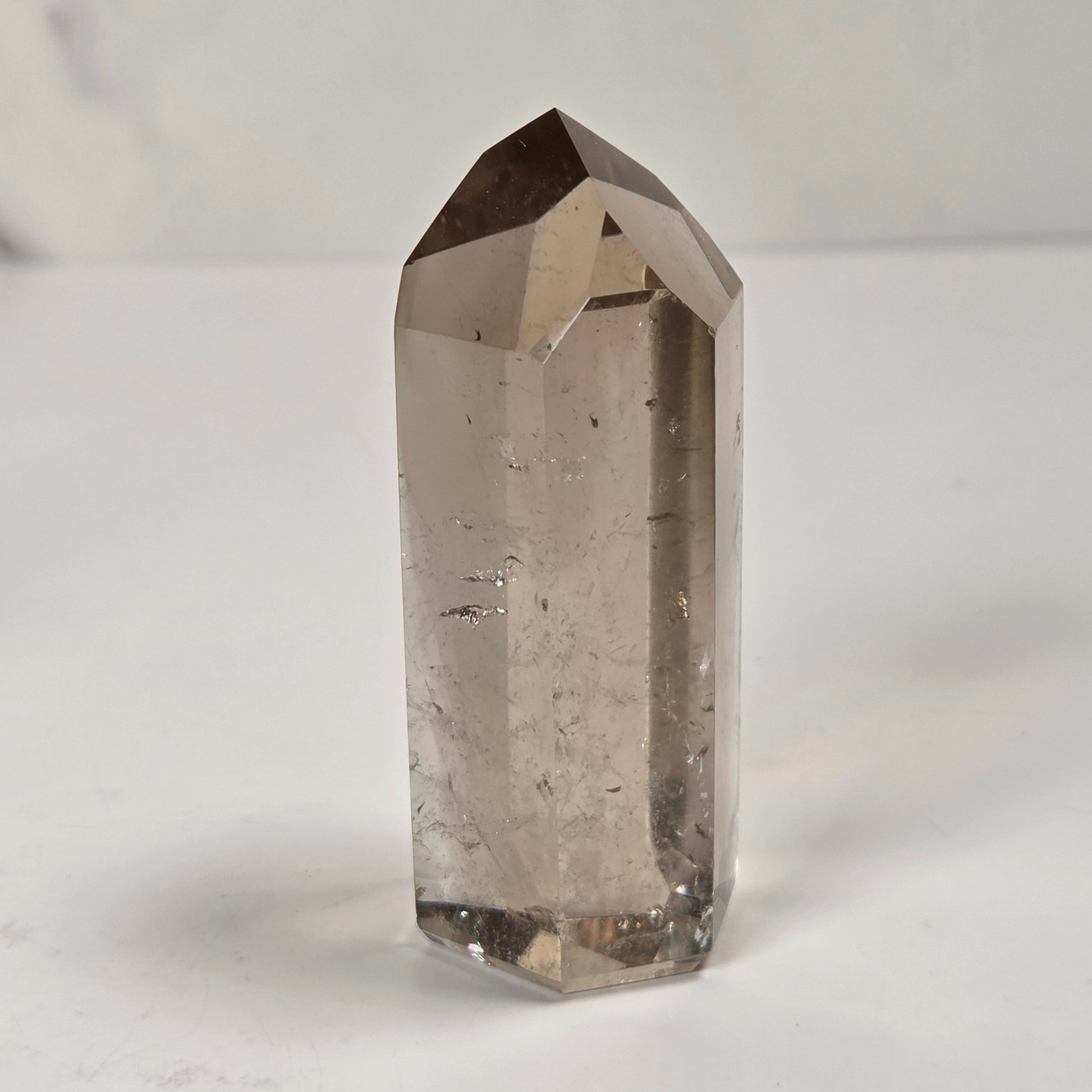 A natural smoky quartz point crystal standing upright on a light gray surface against a white marble background.