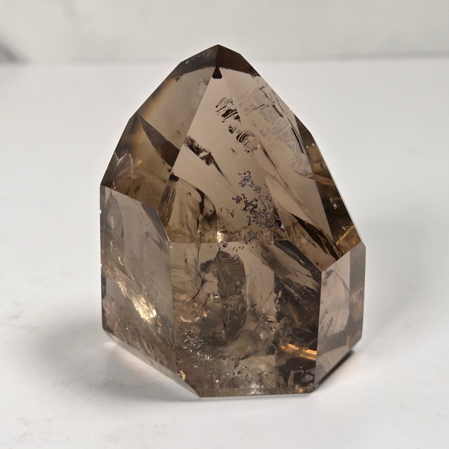 A natural smoky quartz crystal point with internal inclusions, displayed on a light gray surface.