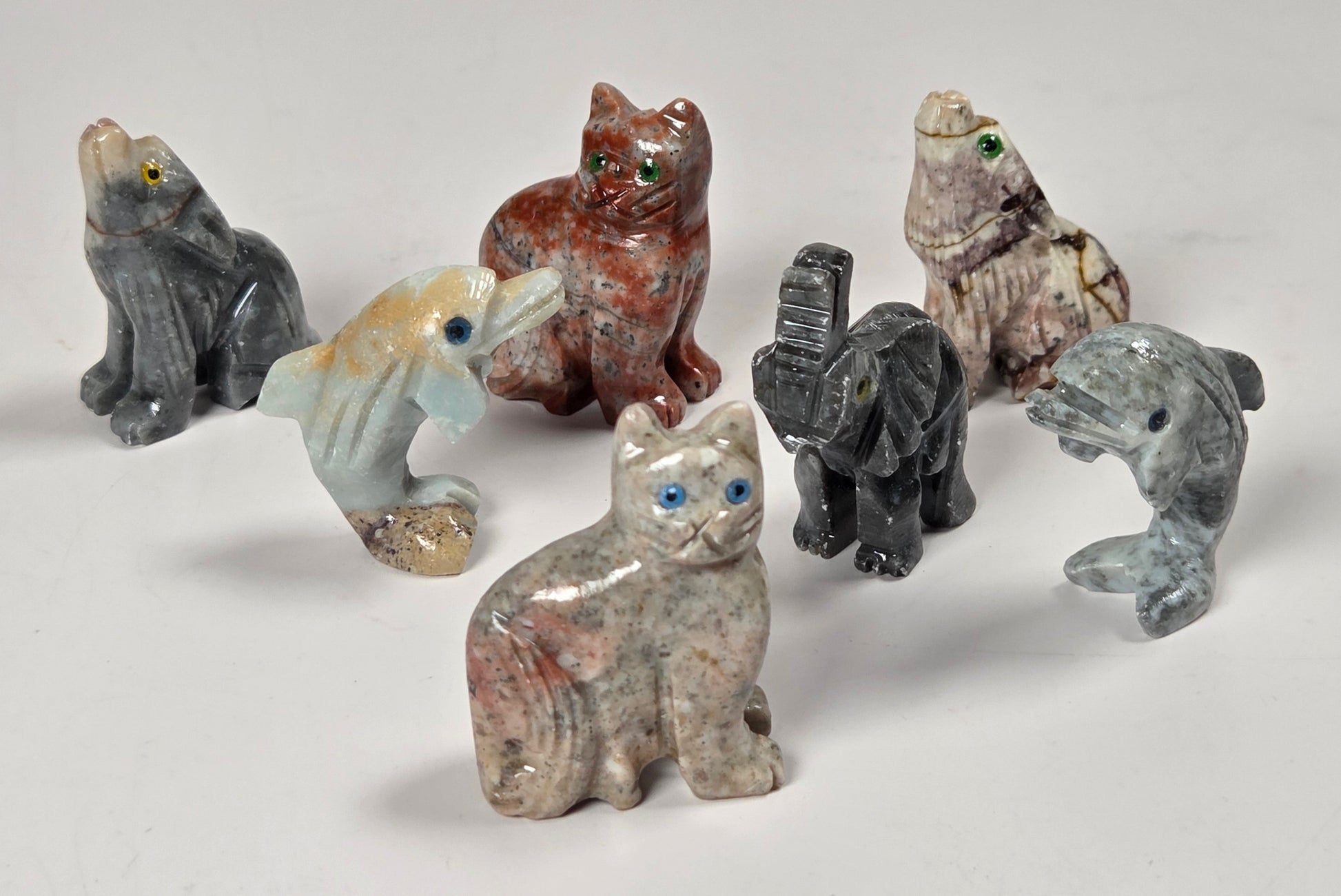 A set of seven small stone carvings of different animals, including a cat, dog, bird, elephant, and dolphin, displayed on a light gray background.