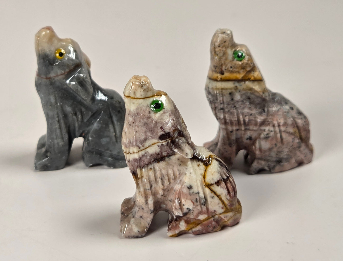 Three small carved stone animal figurines, likely foxes or rabbits, displayed on a light neutral background. The left figure is dark gray with a yellow-green eye.