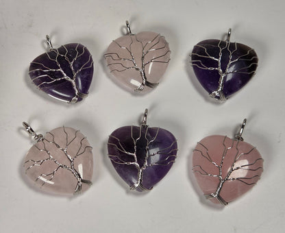 Six heart-shaped crystal pendants arranged in two rows on a light gray background. The pendants feature tree-like silver wire patterns set into polished stones in shades of purple, lavender, and pale pink.