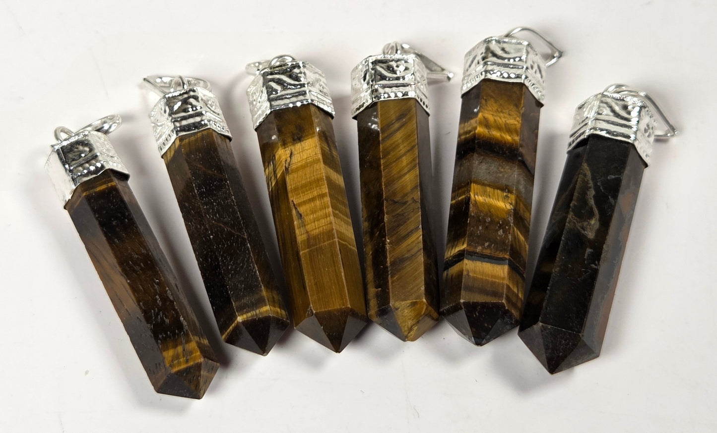 Six pointed tiger's eye crystal pendants with silver caps, arranged in a fan shape on a white background.