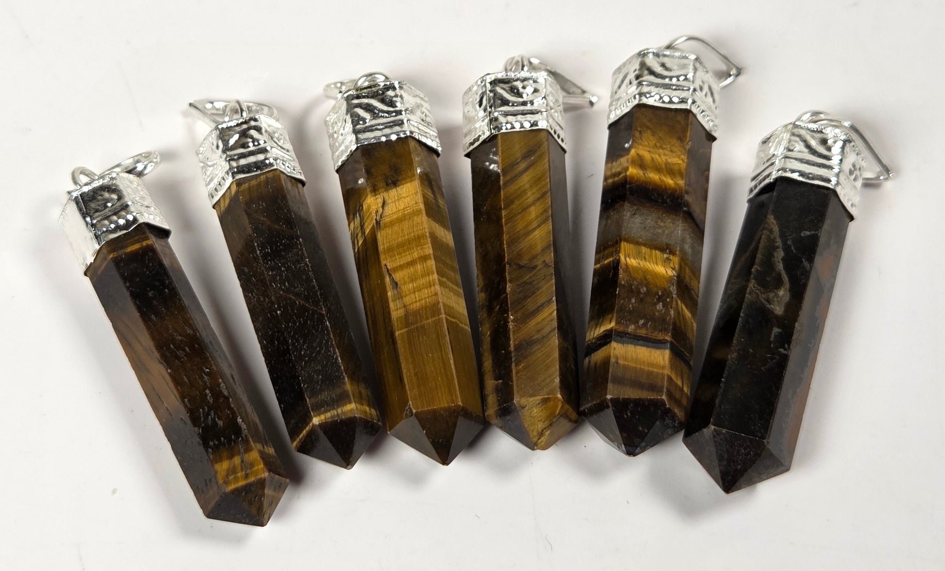 Six pointed tiger's eye crystal pendants with silver caps, arranged in a fan shape on a white background.