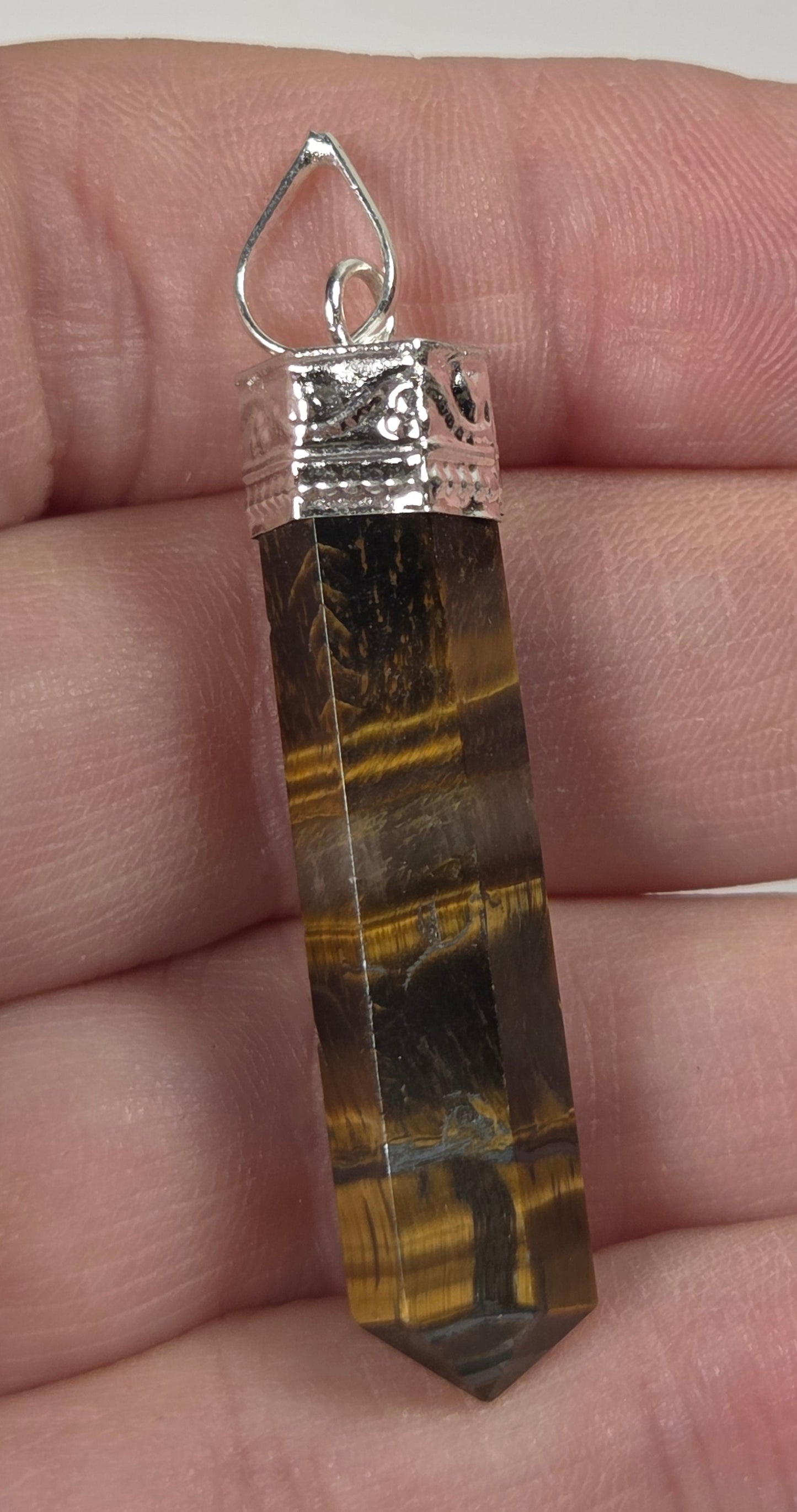 A tiger's eye crystal point pendant with a silver bail, held in a person's hand to show its size.
