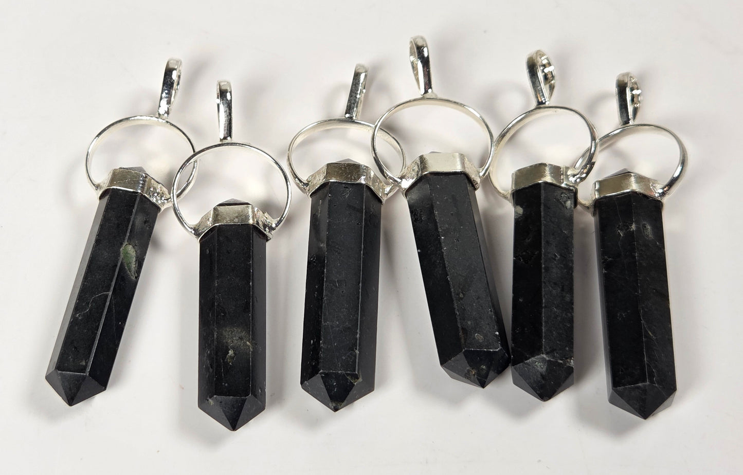 Six black crystal point pendants with silver metal rings and caps, arranged in a row on a plain white background.