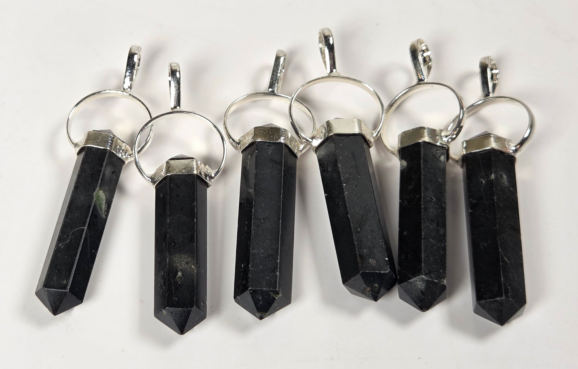 Six black crystal point pendants with silver metal rings and caps, arranged in a row on a plain white background.