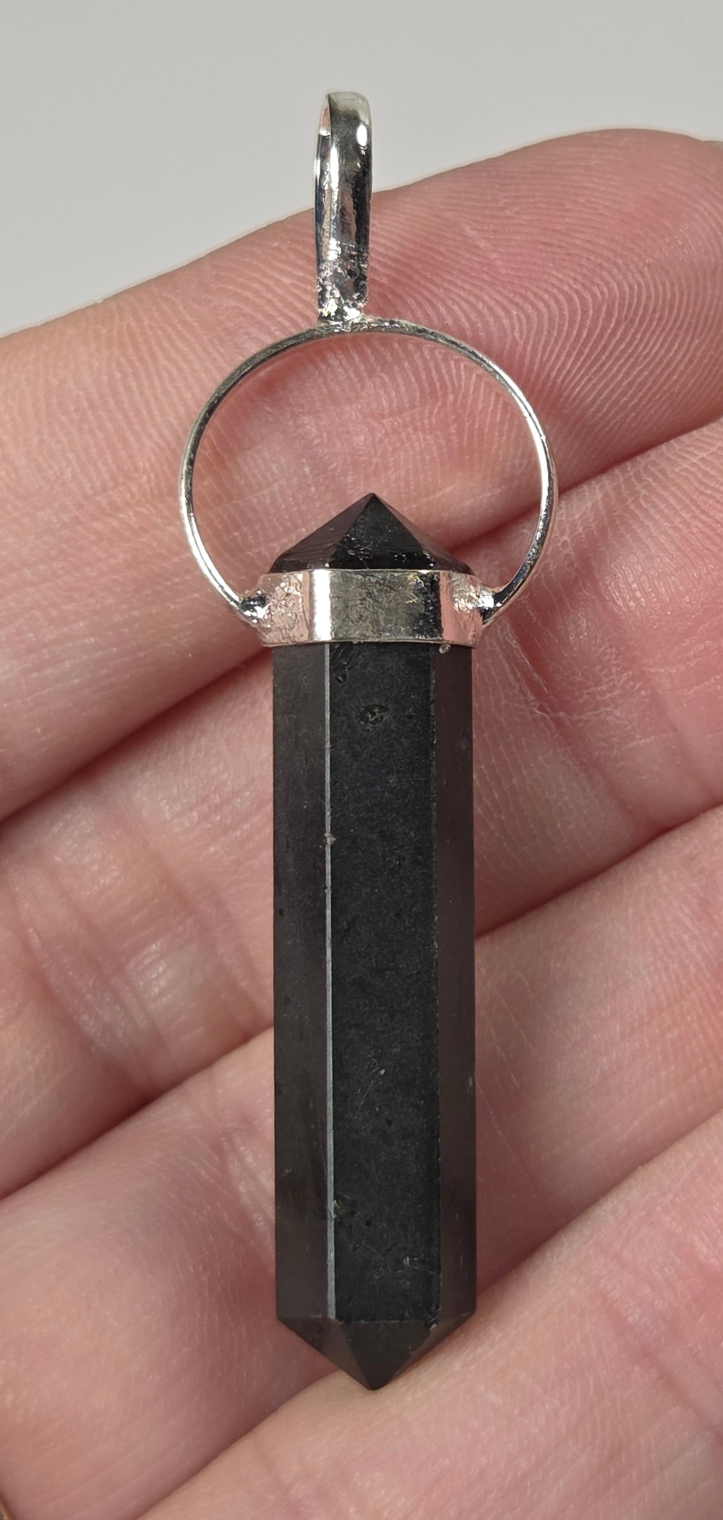 A black crystal point pendant with silver metal caps and a silver keyring, held in a person's hand.