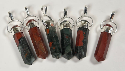 Six faceted crystal pendants with silver-toned metal caps and loops, arranged vertically on a plain white background. The crystals alternate between dark green with red inclusions and reddish-brown with dark inclusions.
