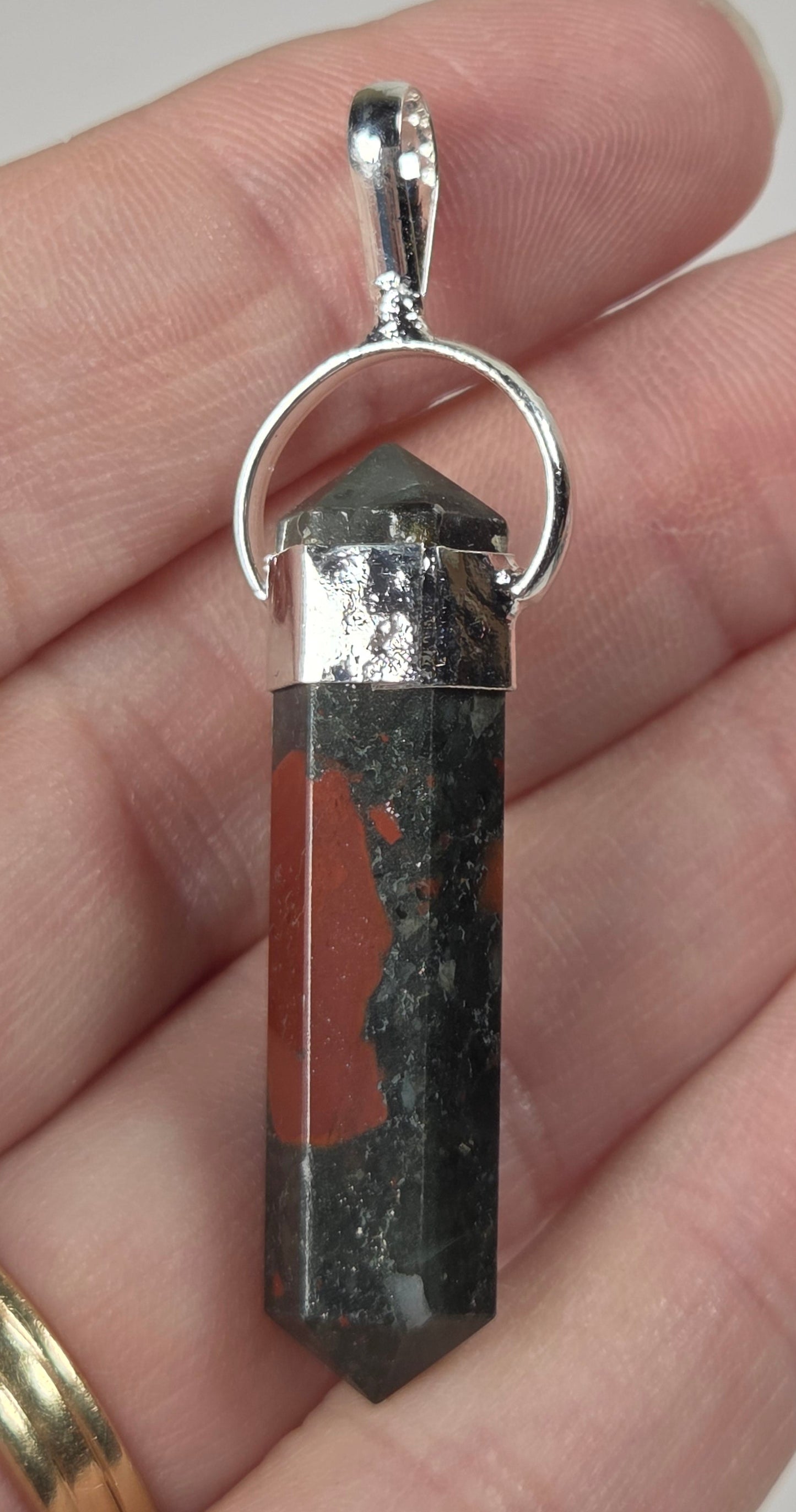 A silver pendant featuring a polished red and black banded stone point, held in a person's hand.