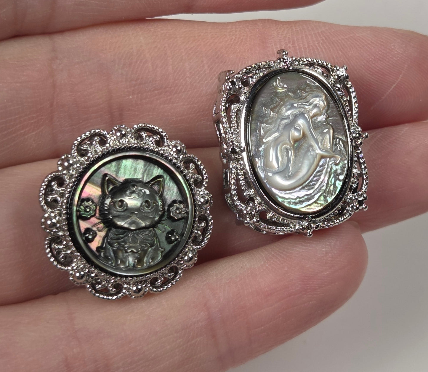 Two silver-toned rings with oval and round cabochon stones, displayed on a person's fingers against a plain light background.