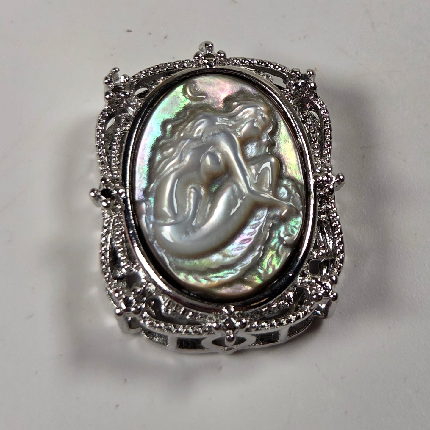 A vintage-style silver ring featuring an oval iridescent mother-of-pearl cabochon with a carved mermaid design, set in an ornate filigree silver band.