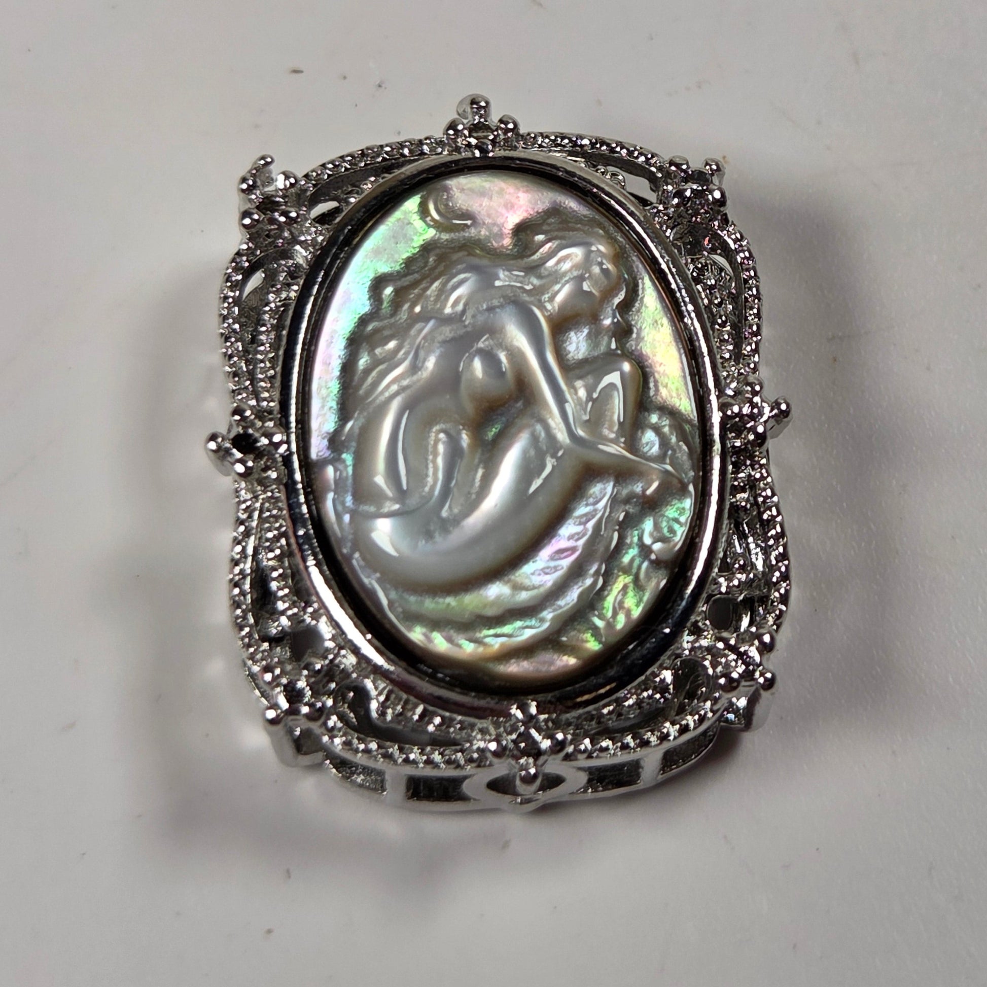 A vintage-style silver ring featuring an oval iridescent mother-of-pearl cabochon with a carved mermaid design, set in an ornate filigree silver band.