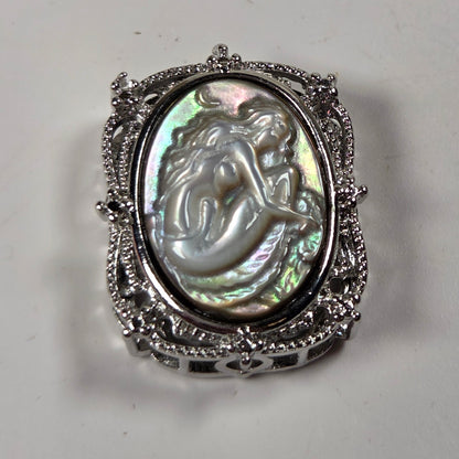 A vintage-style silver ring featuring an oval iridescent mother-of-pearl cabochon with a carved mermaid design, set in an ornate filigree silver band.