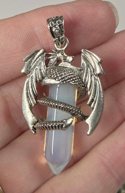 A silver dragon pendant with a pale lavender-white crystal point, held in a person's hand.