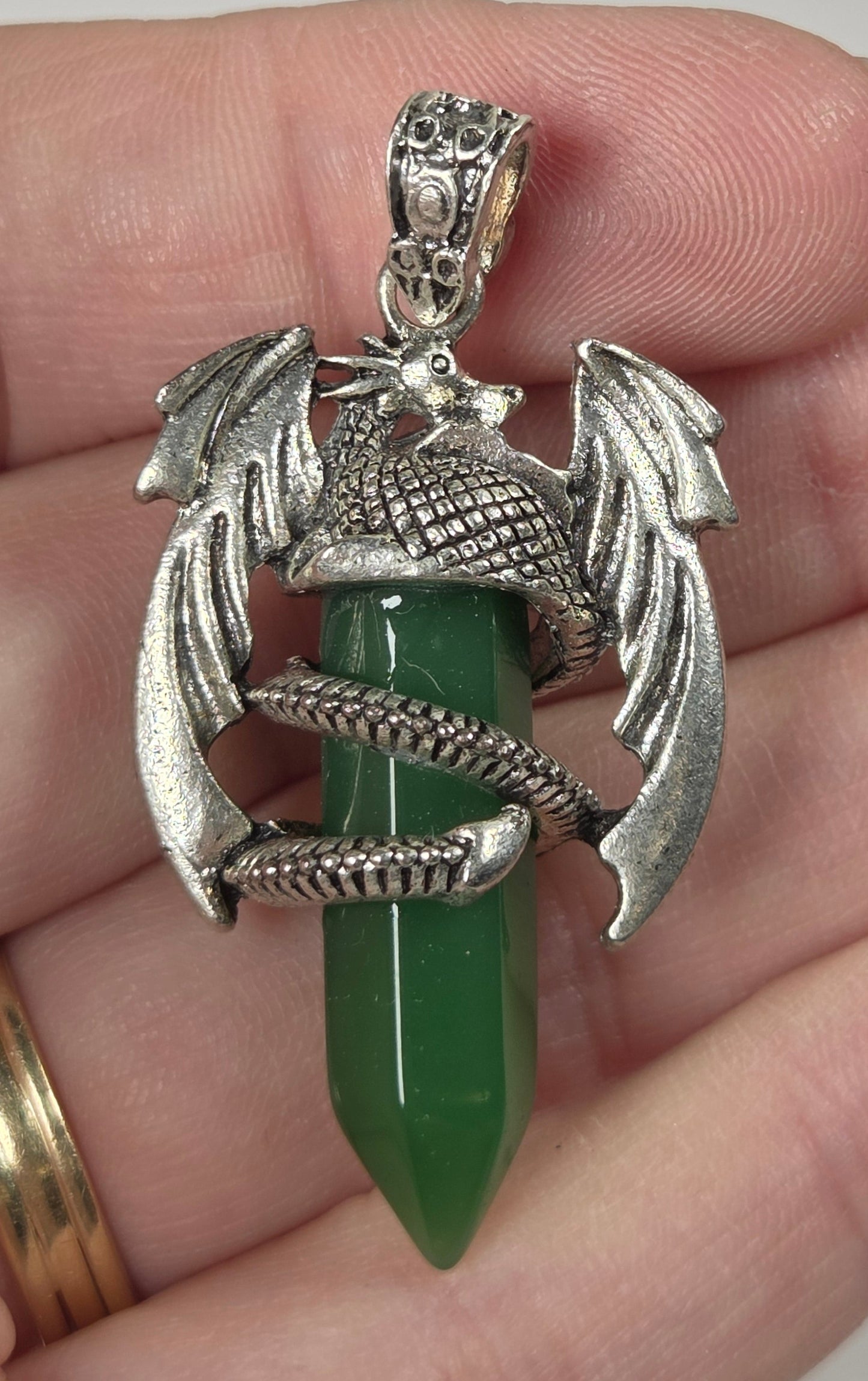 A close-up of a hand holding a silver-toned dragon pendant wrapped around a green crystal point.
