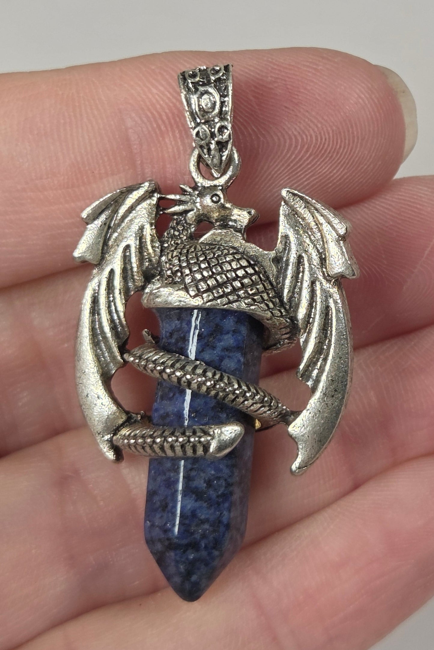 A hand holding a silver-toned dragon pendant with a blue lapis lazuli crystal point.