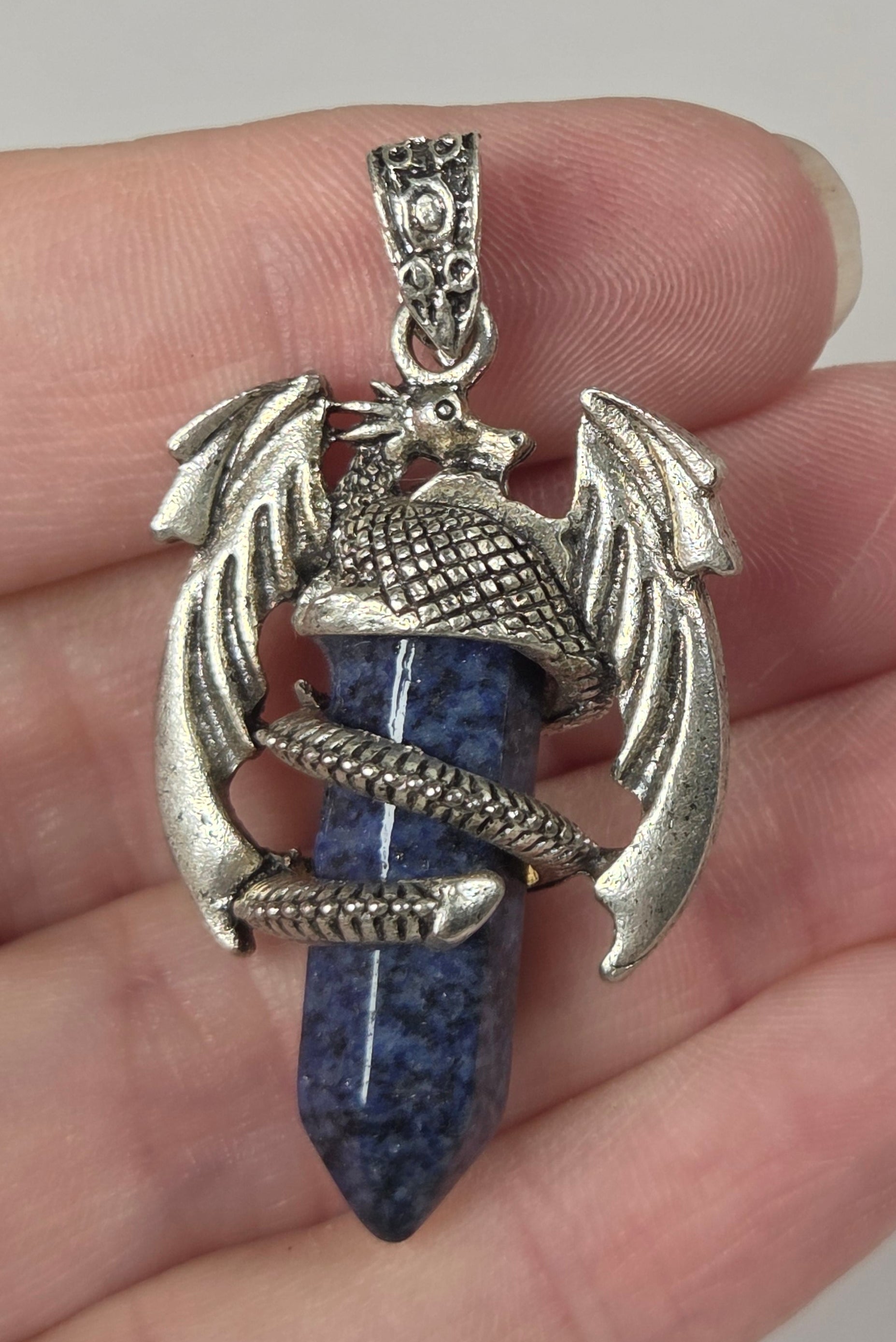 A hand holding a silver-toned dragon pendant with a blue lapis lazuli crystal point.