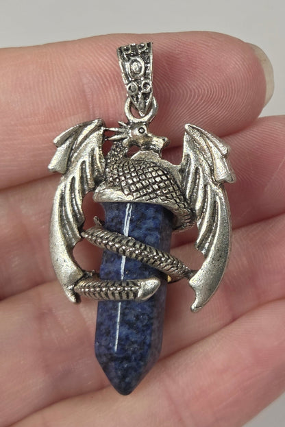 A hand holding a silver-toned dragon pendant with a blue lapis lazuli crystal point.