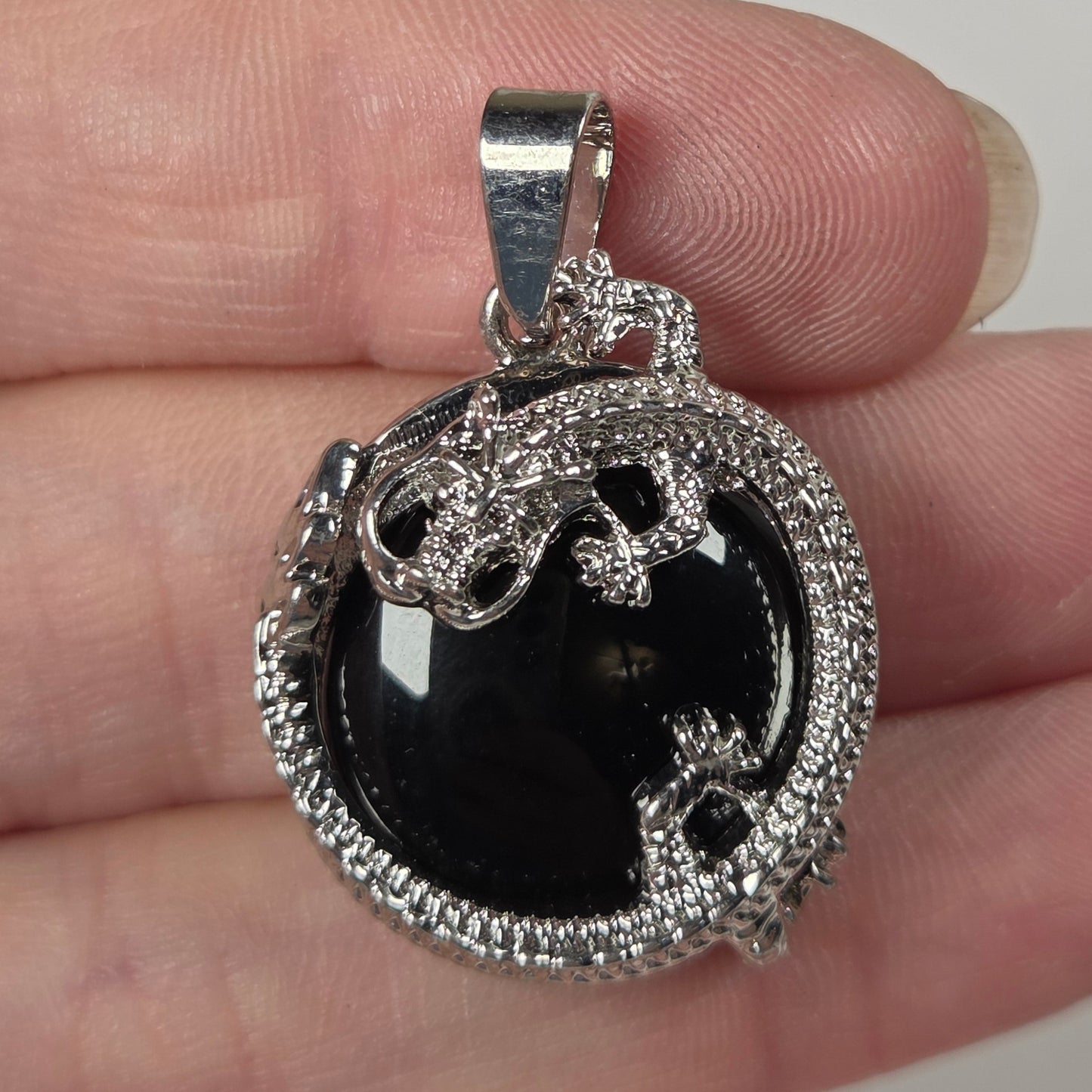 A close-up of a hand holding a silver pendant with a black oval center stone and a border of small clear stones.