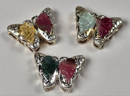 Three butterfly-shaped earrings with silver-toned metal borders, clear rhinestones, and colorful inlay wings in green, yellow, pink, and light blue, arranged on a light gray background.
