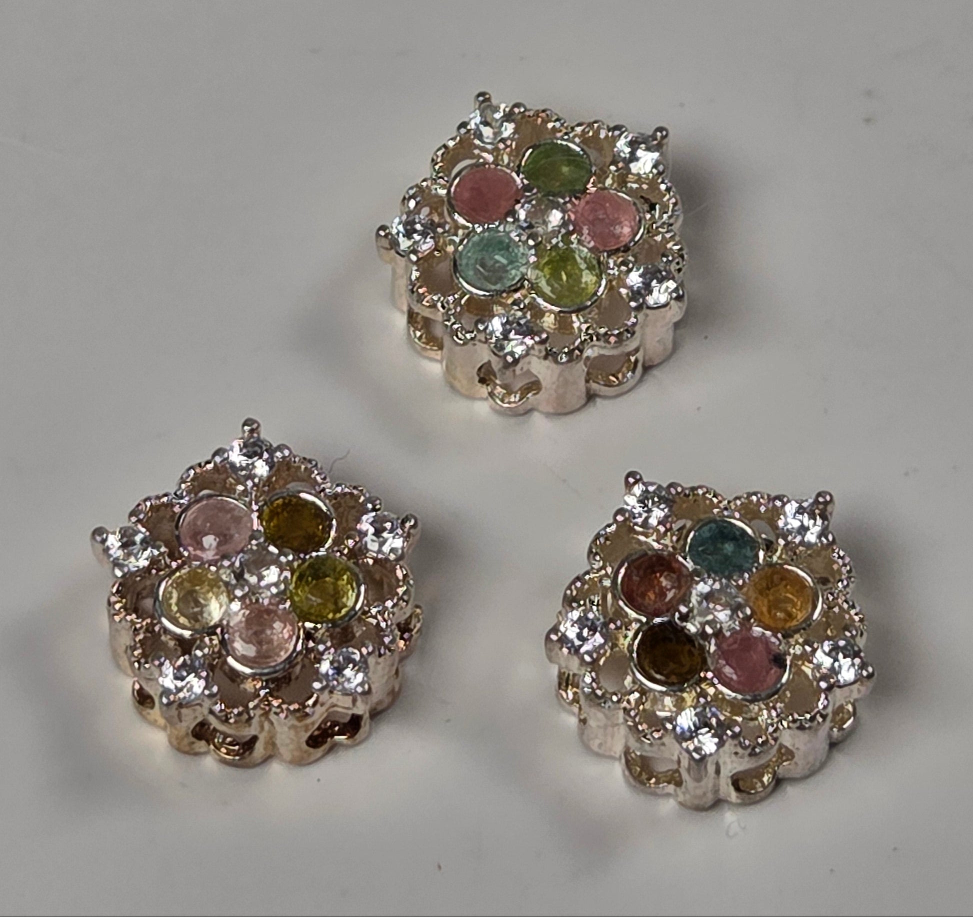 Three silver-toned floral bead spacers with multicolored round crystals, arranged on a light gray surface.