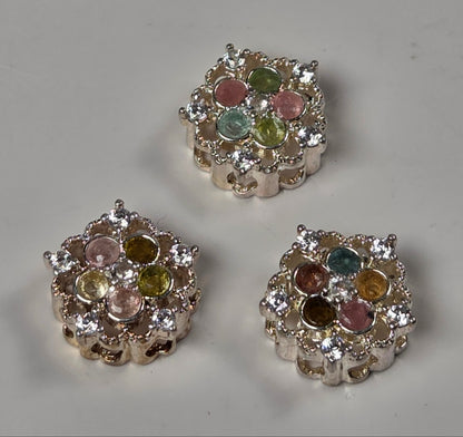 Three silver-toned floral bead spacers with multicolored round crystals, arranged on a light gray surface.