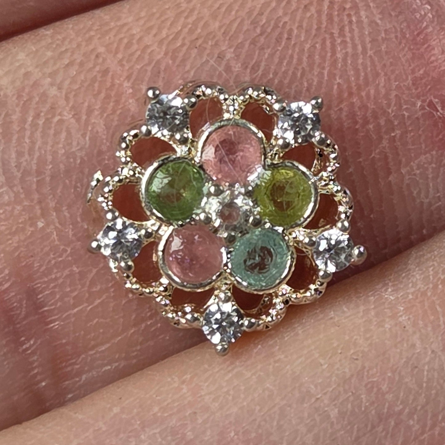 A close-up of a silver-toned ring with five round gemstones in pastel pink, green, and blue, displayed on a person's finger.