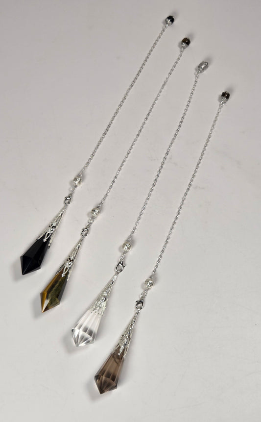 Four crystal and silver chain pendulums laid out diagonally on a light gray background. The pendulums feature faceted crystal drops in black, smoky brown, clear, and olive-brown tones, connected by delicate silver chains with small silver beads.