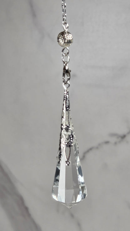 A silver-toned chain accessory with a faceted clear crystal pendant, displayed horizontally against a light gray marble background.