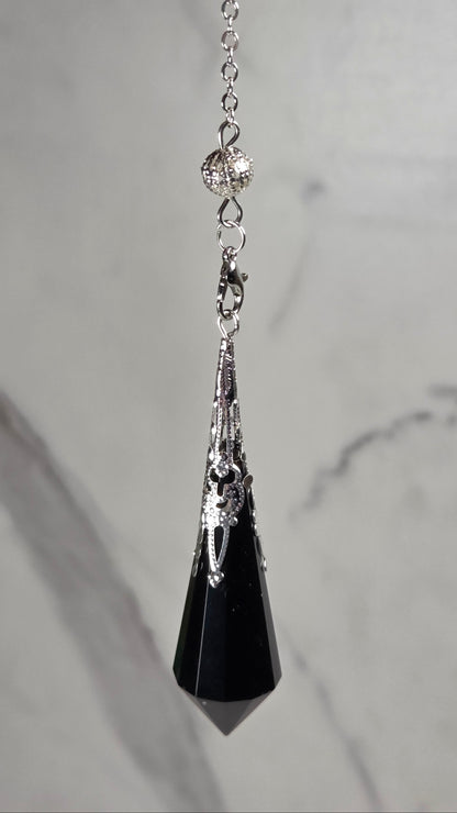 A silver-toned chain pendulum with a black faceted crystal pendant, displayed on a light gray marble surface.